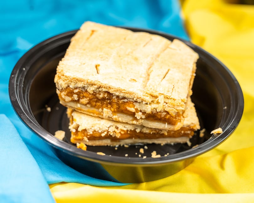 Two pieces of pumpkin pie in a black bowl, set against a blue and yellow fabric background.