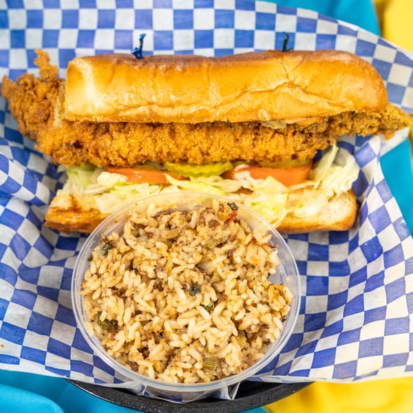 Crispy fried chicken po'boy with lettuce, tomato, and pickles, served with a side of dirty rice.
