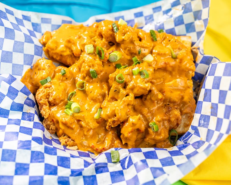Crispy fried chicken pieces coated in a rich orange sauce and garnished with green onions in a checkered basket.