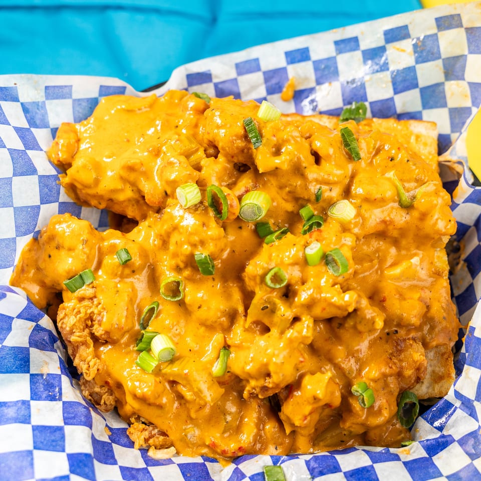 Crispy fried chicken covered in a creamy orange sauce and green onions, served in a checkered basket.