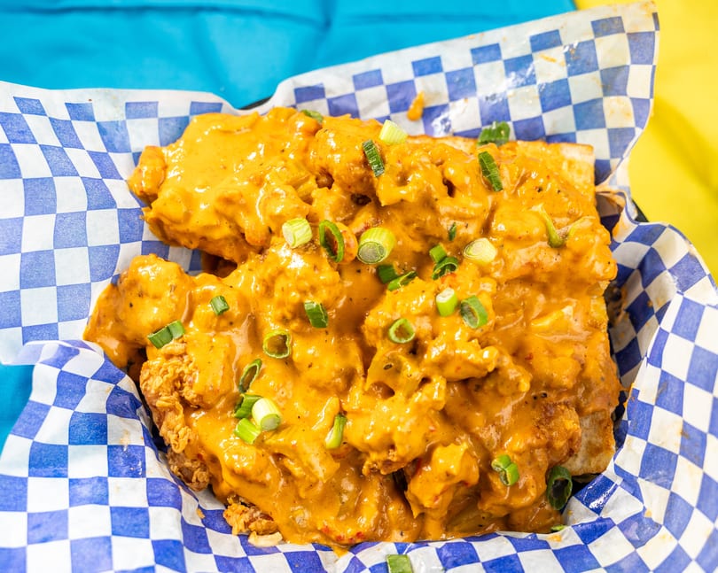 Crispy fried chicken covered in a creamy orange sauce and green onions, served in a checkered basket.