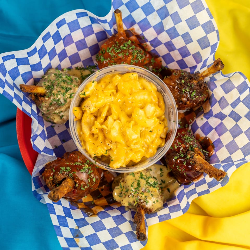 A basket of chicken lollipops with various sauces and a side of mac and cheese.