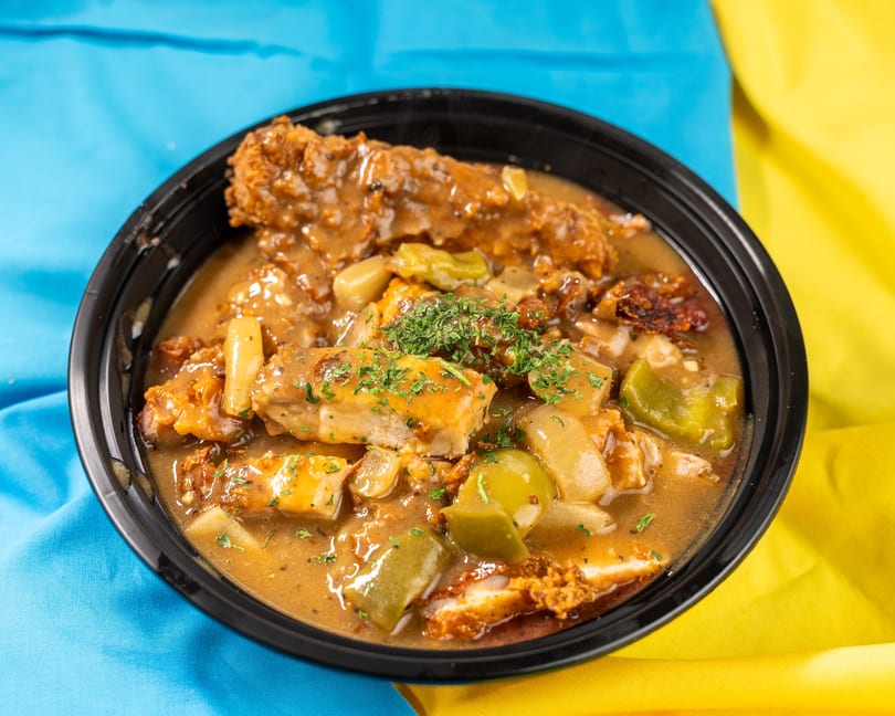 Hearty chicken and gravy with peppers and onions, garnished with parsley in a black bowl.