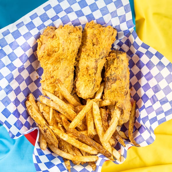 Three pieces of fried fish and a pile of french fries in a blue and white checkered basket.